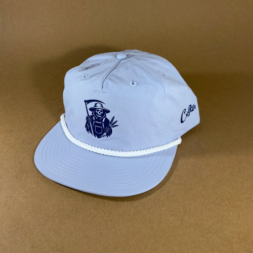 A light blue flat-brim cap with a white braided rope around the brim, featuring a dark blue embroidered grim reaper farmer graphic on the front and the word 'Crofter' on the side.