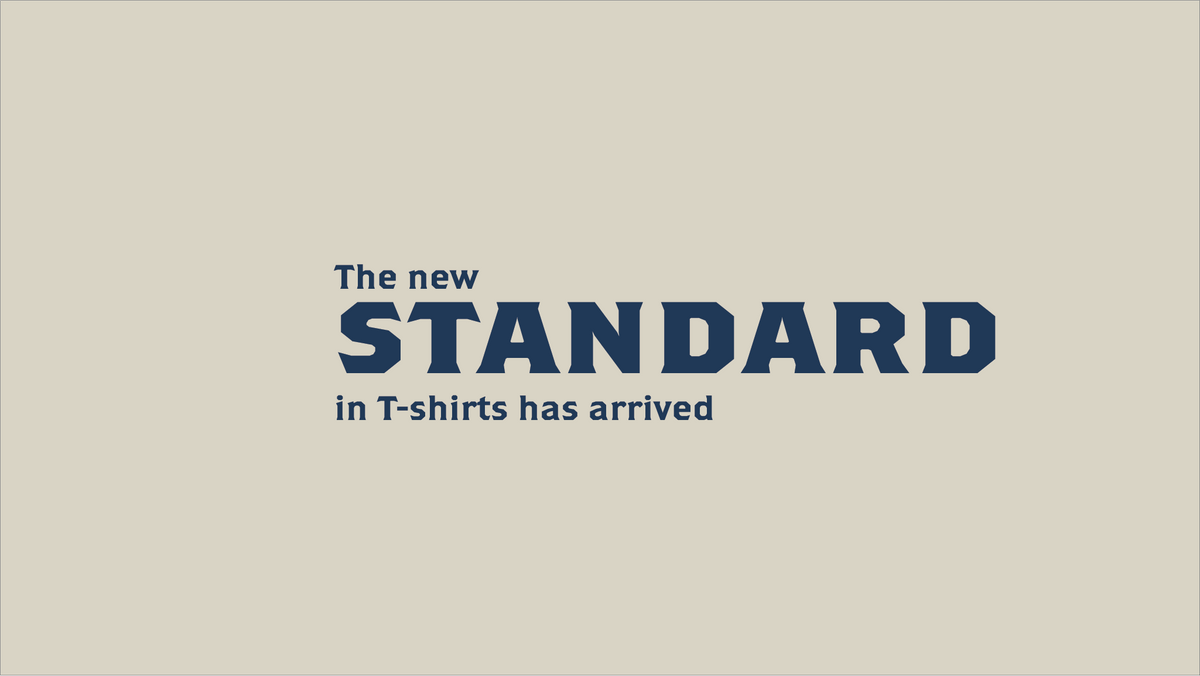 A minimalist graphic with the text "The new STANDARD in T-shirts has arrived" in dark navy blue on a warm beige background.